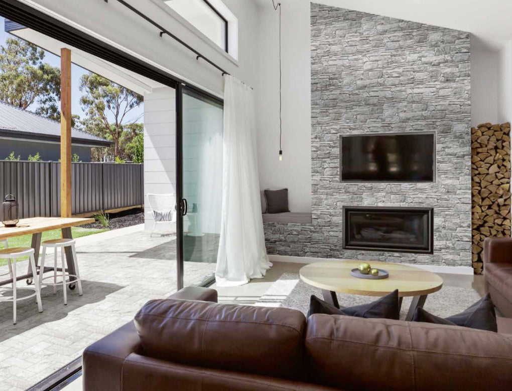 Vulcani Grigio 160x400mm grey stacked stone tiles cladding a floor-to-ceiling fireplace feature wall in a modern living room with leather sofa and mounted TV.