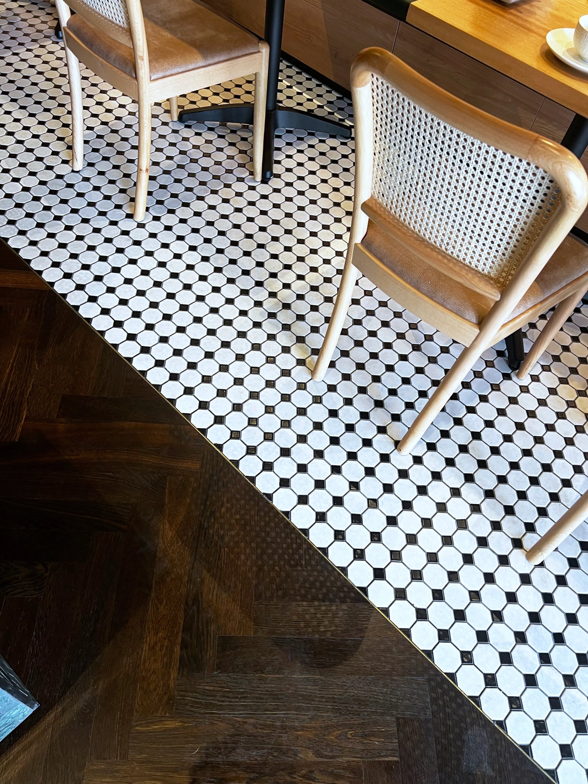 White and Black Matte Porcelain Glazed Octagon Small tiles installed on a restaurant floor beside dark herringbone parquet wood flooring with rattan dining chairs.