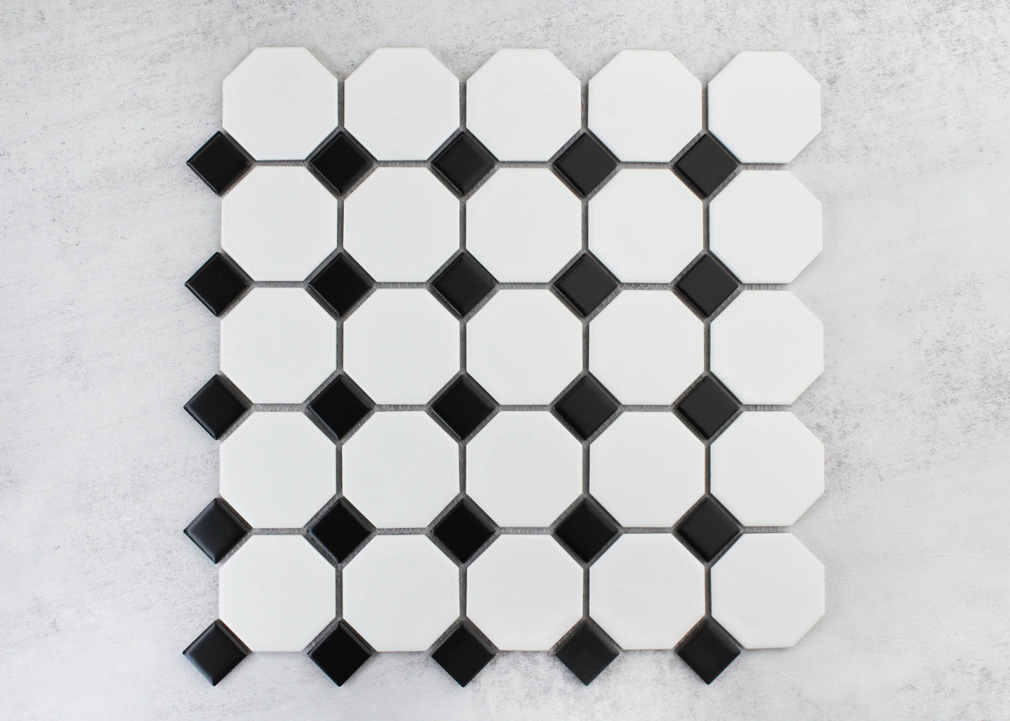 Flat lay pack shot of White and Black Matte Porcelain Glazed Octagon Small tiles showing white octagonal shapes with black diamond dot accents on a grey surface.