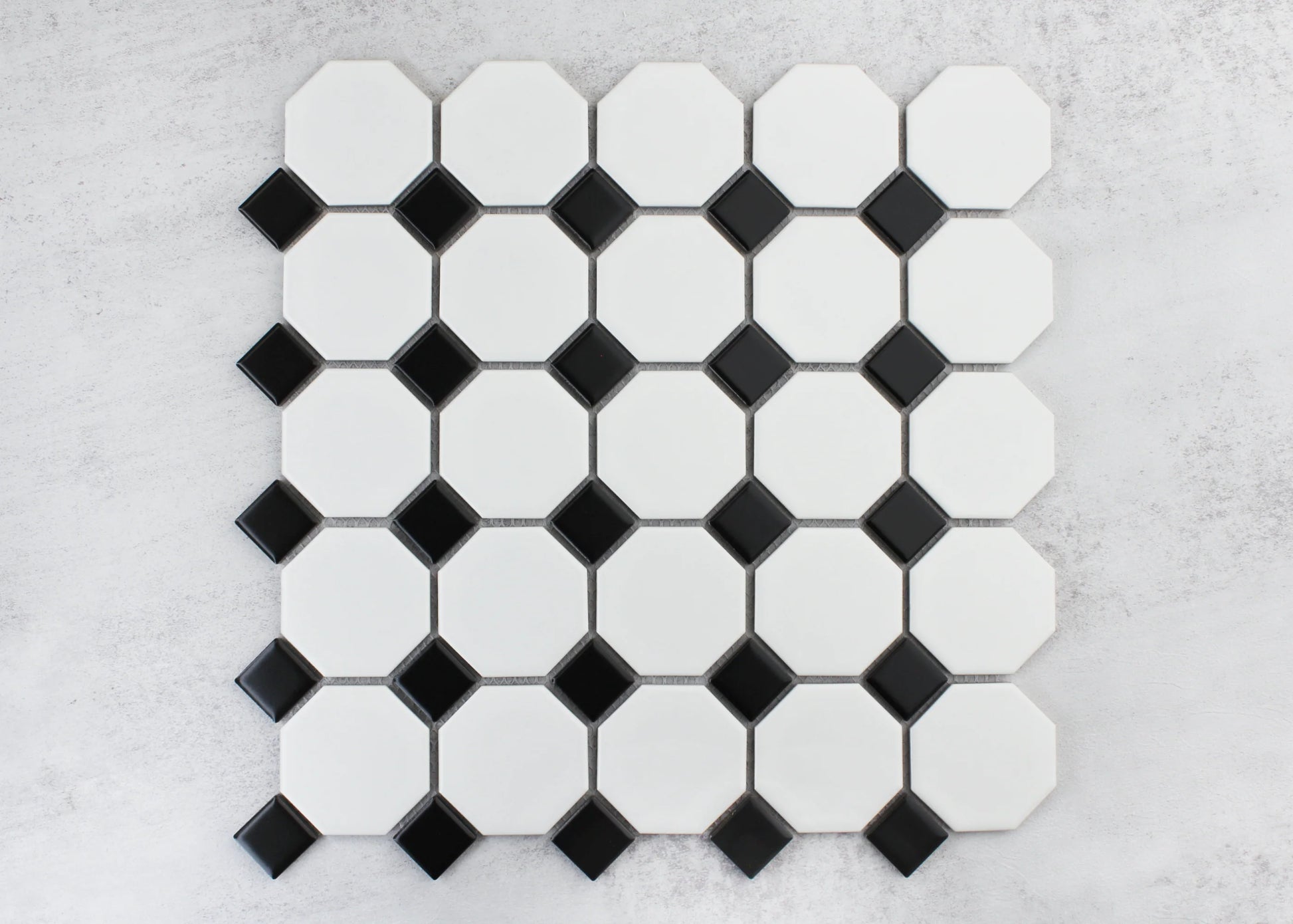 Flat lay pack shot of White and Black Matte Porcelain Glazed Octagon Small tiles showing white octagonal shapes with black diamond dot accents on a grey surface.