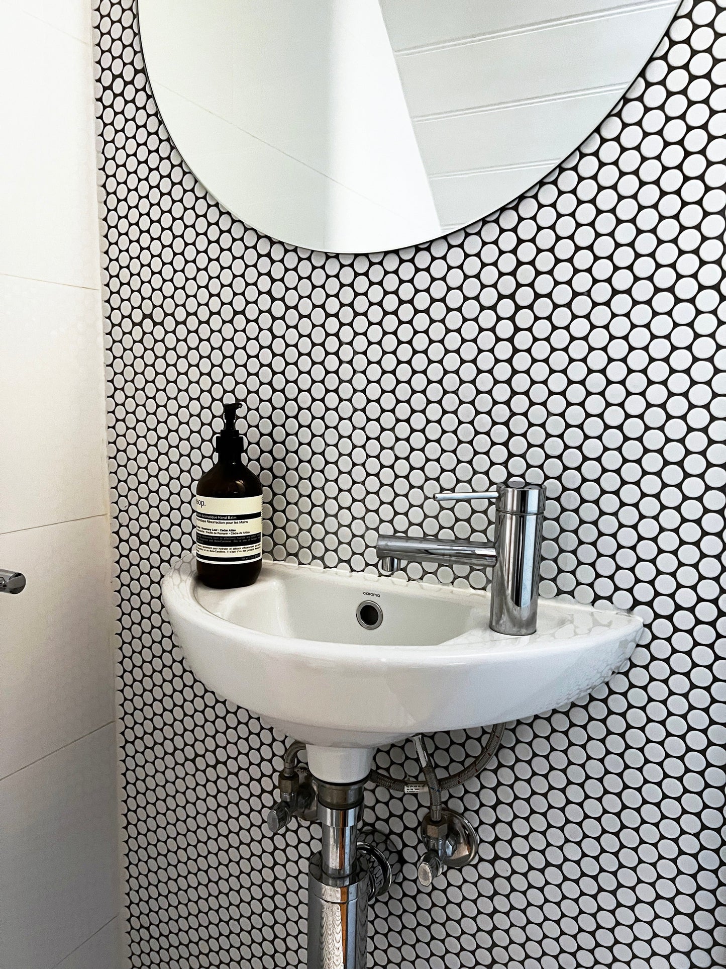 White Gloss Diameter Glazed Porcelain Penny Round 19mm tiles covering a bathroom feature wall behind a wall-mounted basin with chrome tap and Aesop hand soap dispenser.