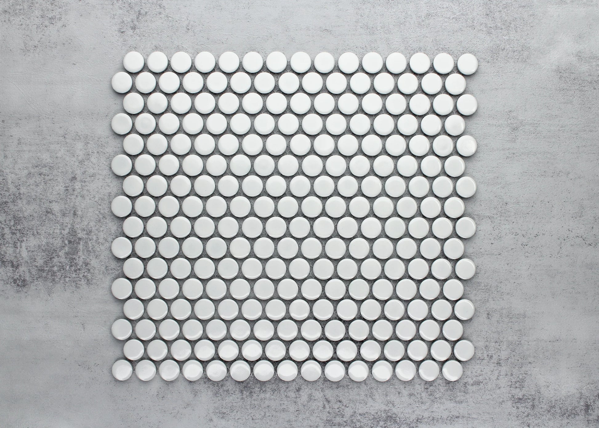 Flat lay pack shot of White Gloss Diameter Glazed Porcelain Penny Round 19mm tiles arranged in a uniform grid pattern on a grey concrete surface.
