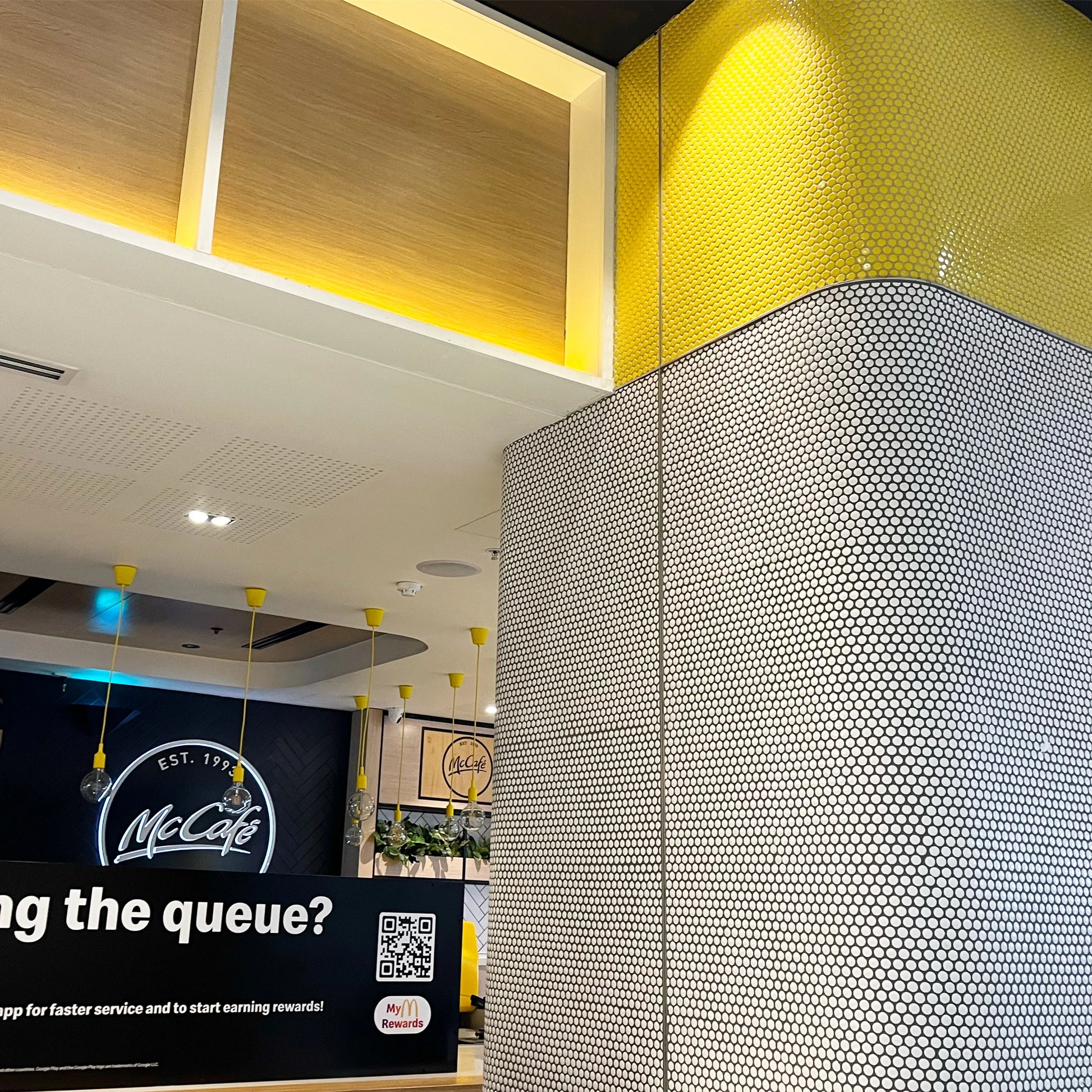 White Gloss Diameter Glazed Porcelain Penny Round 19mm tiles installed on a curved column inside a modern McCafe restaurant with yellow pendant lighting.