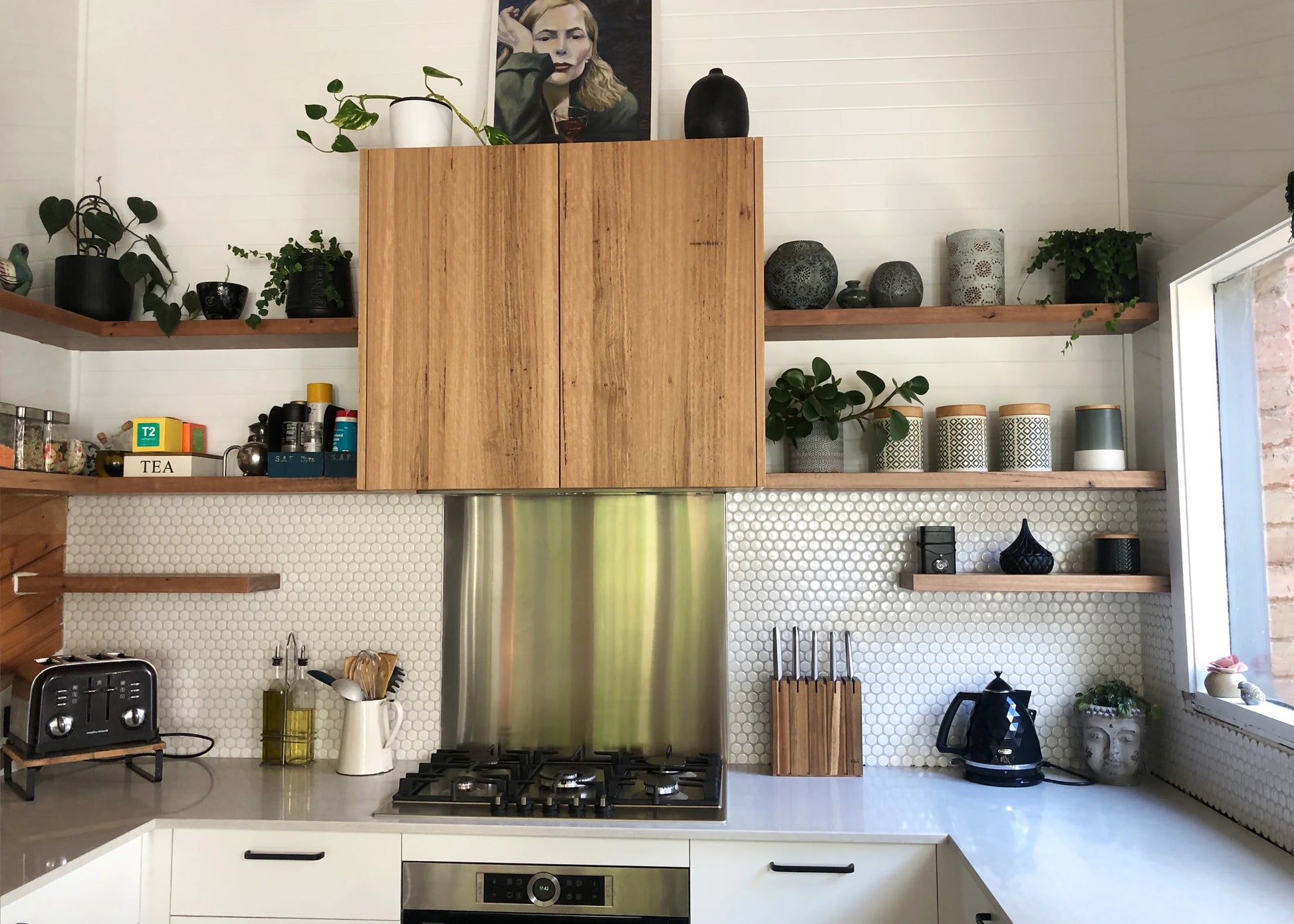 White Gloss Glazed Porcelain Penny Round 28mm Diameter tiles installed as a kitchen splashback with open timber shelving, gas cooktop, and decorative plants.