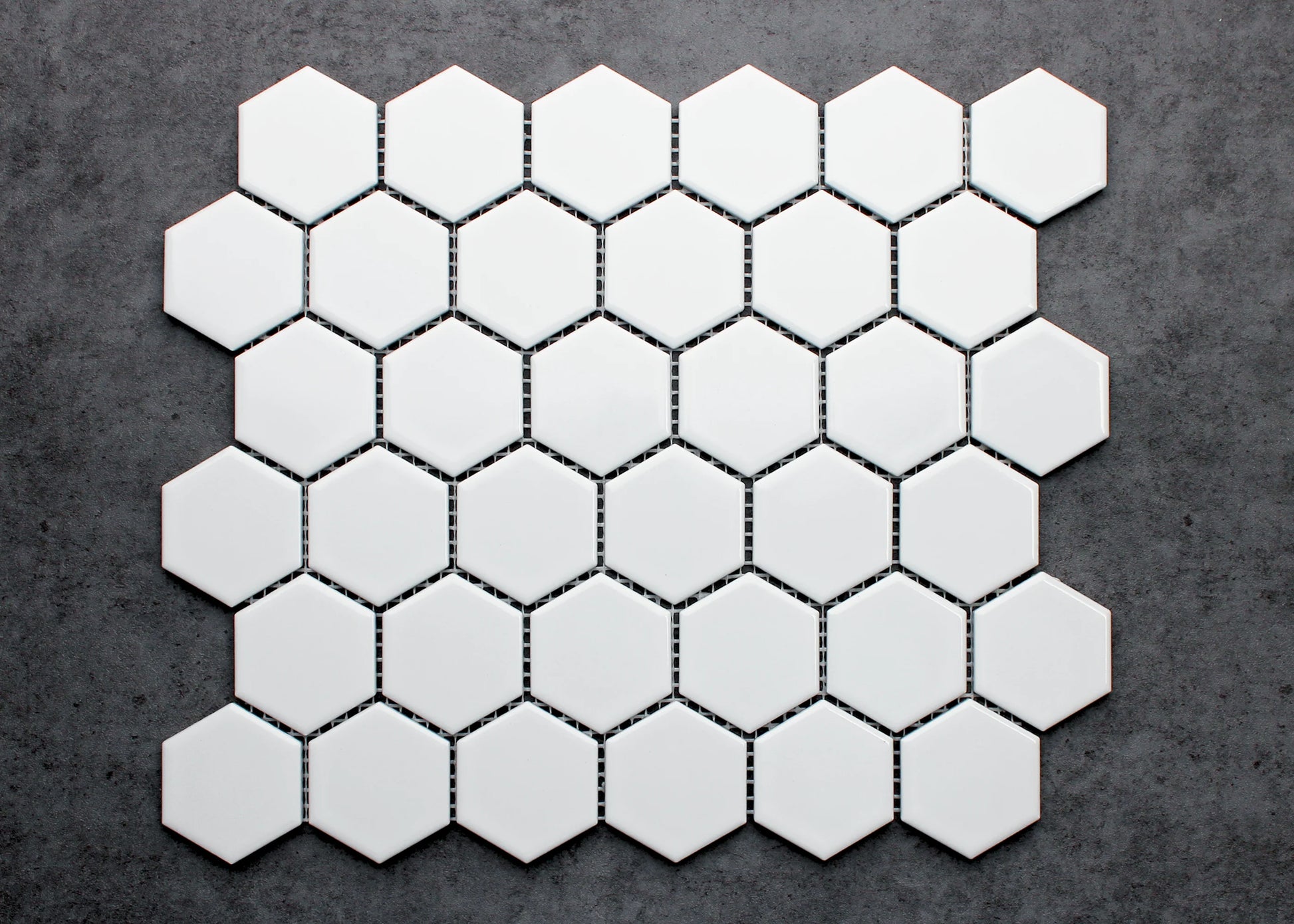 White Gloss Porcelain Glazed Hexagon 51x59mm mosaic sheet displayed flat against a dark grey concrete background, showing uniform white glazed finish and tight grout spacing.
