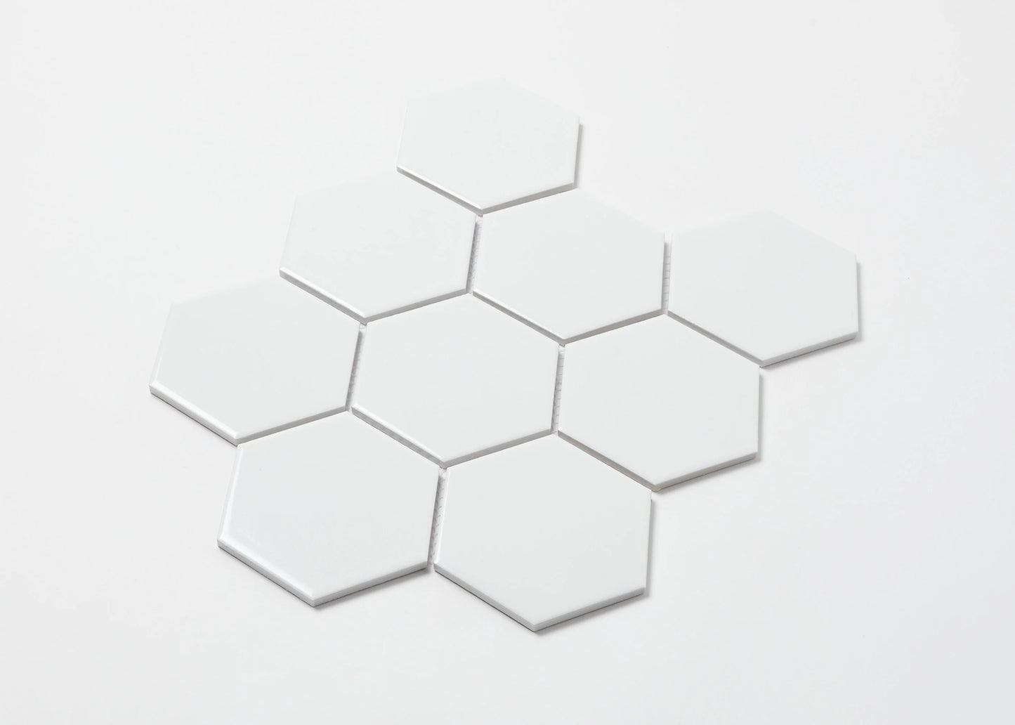 White Gloss Porcelain Glazed Hexagon 95x110mm tiles arranged in a loose cluster formation showing their glossy white finish and uniform hexagonal shape against a white background.