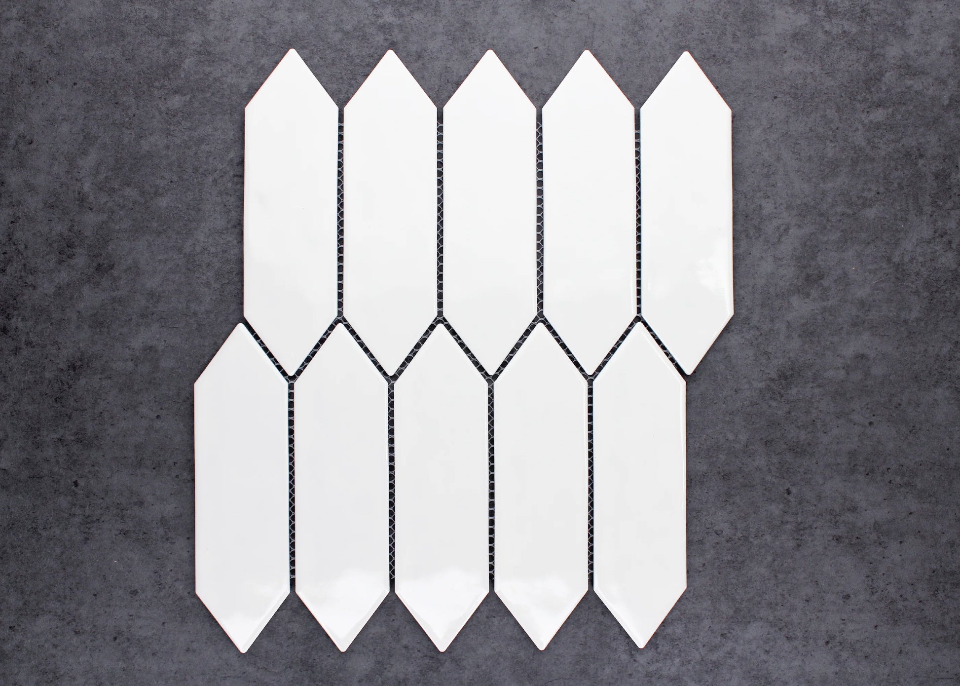 White Gloss Porcelain Glazed Ripple Surface Arrow 55x195mm tiles arranged in an interlocking staggered pattern showing glossy white elongated arrow-shaped ceramic pieces against a dark grey background.