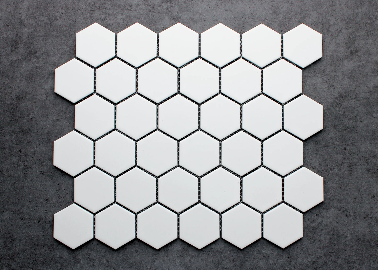 White Matt Porcelain Glazed Hexagon 51x59mm mosaic sheet laid flat on a dark grey concrete surface, showing the matte white finish and uniform hexagonal pattern.