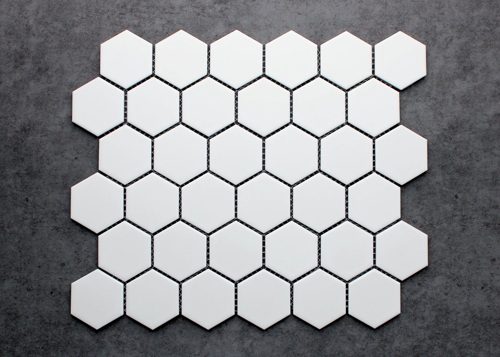 White Matt Porcelain Glazed Hexagon 51x59mm mosaic sheet laid flat on a dark grey concrete surface, showing the matte white finish and uniform hexagonal pattern.