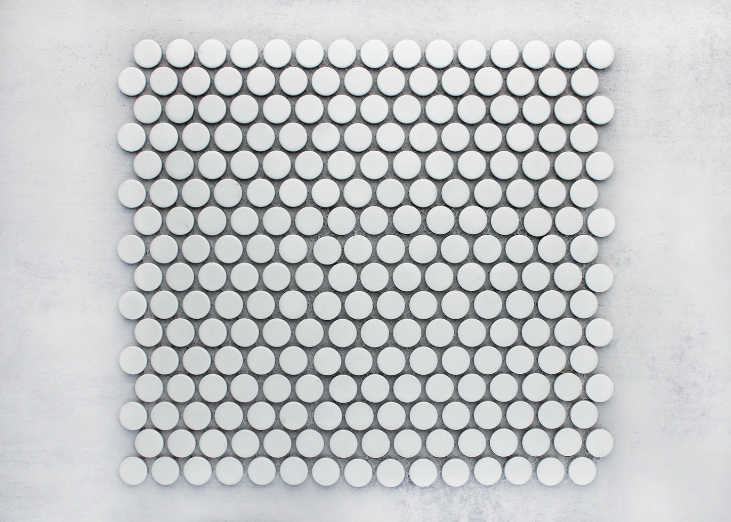 Flat lay pack shot of White Matte Glazed Porcelain Penny Round 19mm Diameter tiles arranged in a uniform grid pattern on a light grey surface.