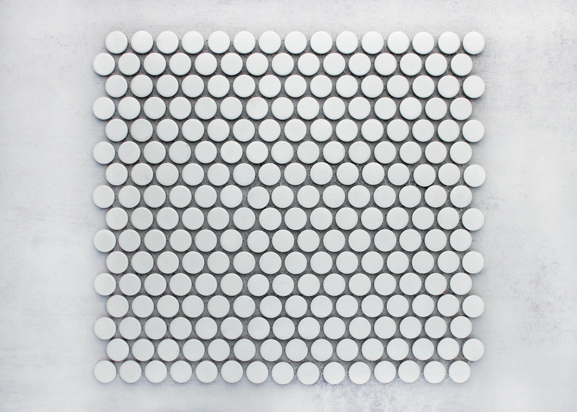 Flat lay pack shot of White Matte Glazed Porcelain Penny Round 19mm Diameter tiles arranged in a uniform grid pattern on a light grey surface.