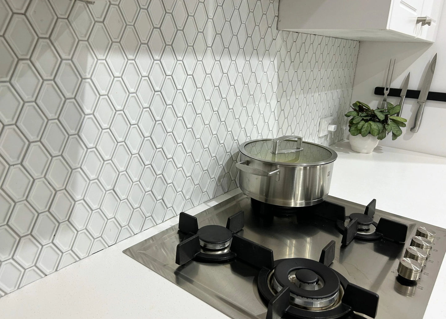 White Matte Internal Porcelain Glazed Honeycombe Internal 46.5x60mm installed as a kitchen splashback behind a stainless steel gas cooktop with a pot and magnetic knife strip.