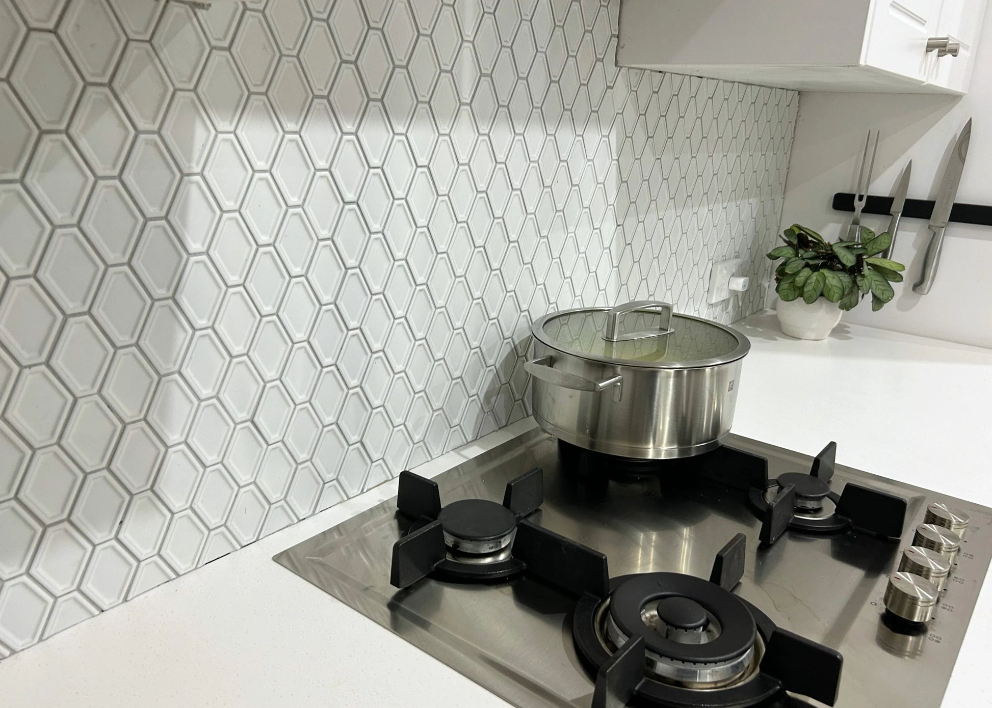 White Matte Internal Porcelain Glazed Honeycombe Internal 46.5x60mm installed as a kitchen splashback behind a stainless steel gas cooktop with a pot and magnetic knife strip.