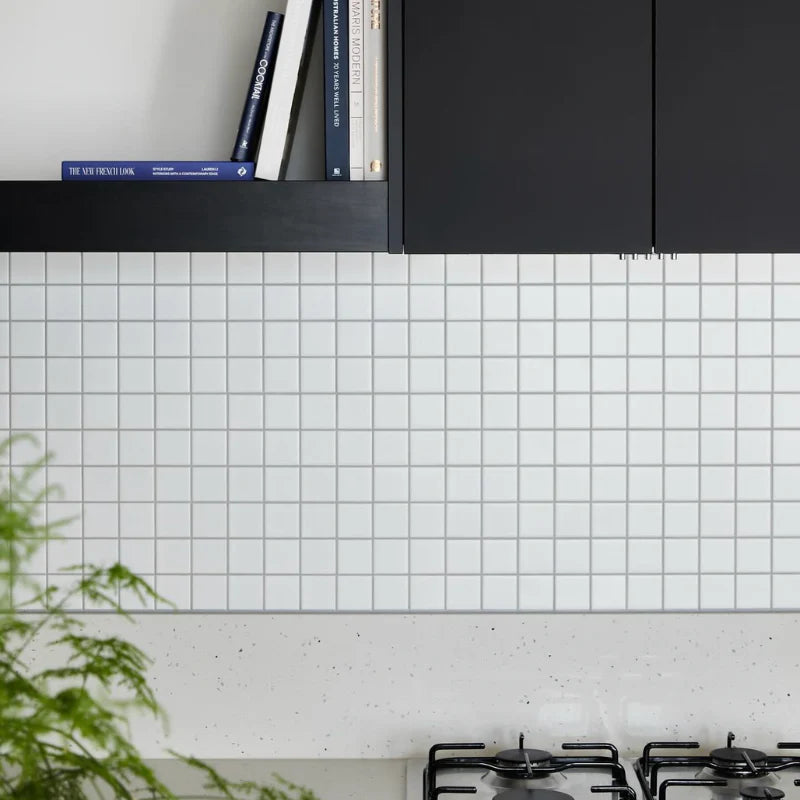 White Matte Porcelain Glazed 48x48mm Square tiles installed as a kitchen splashback beneath dark matte cabinetry with a speckled stone benchtop and gas cooktop.