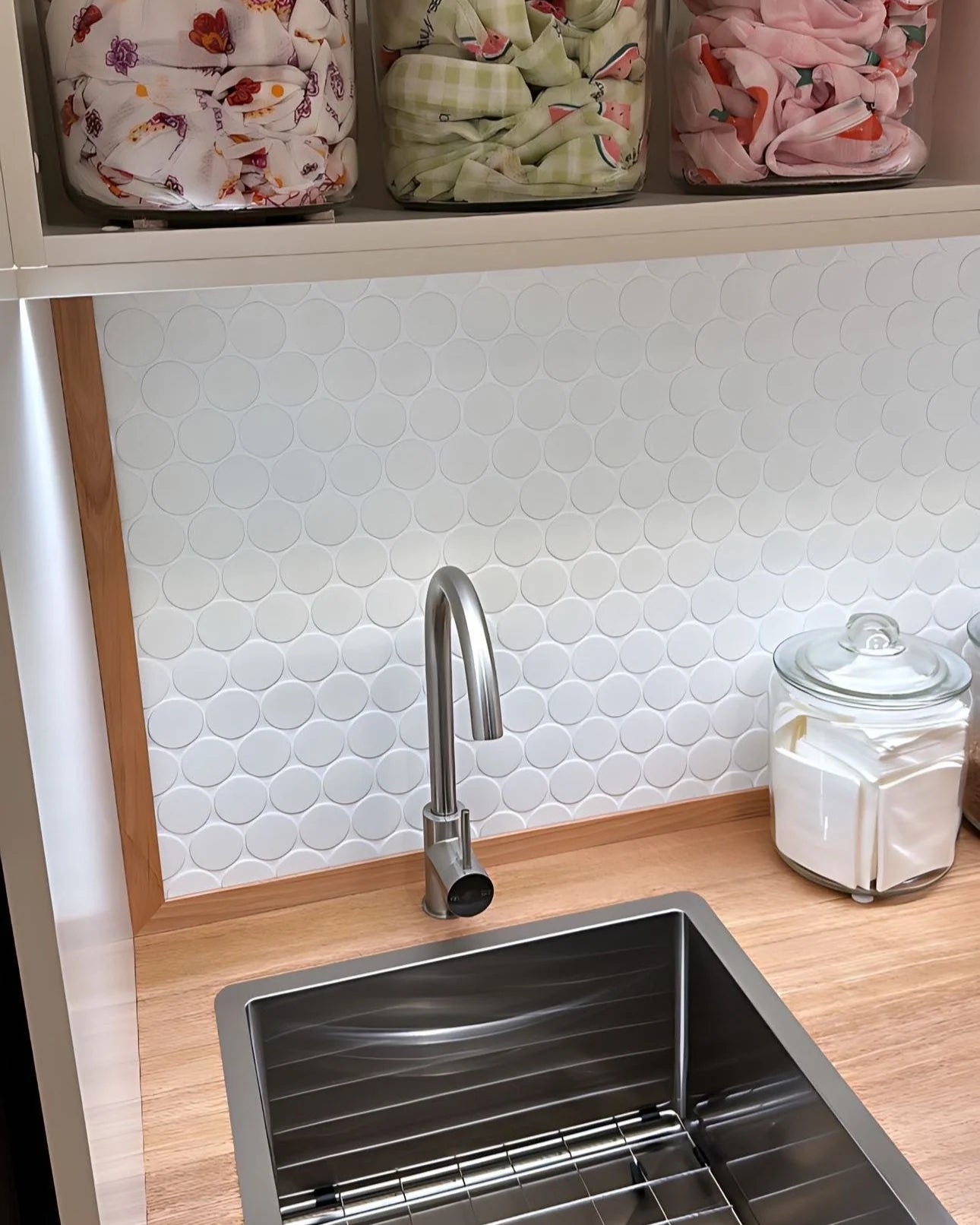 White Matte Porcelain Glazed Penny Round 48mm tiles installed as a splashback behind a stainless steel sink and faucet in a modern laundry room with timber benchtop.