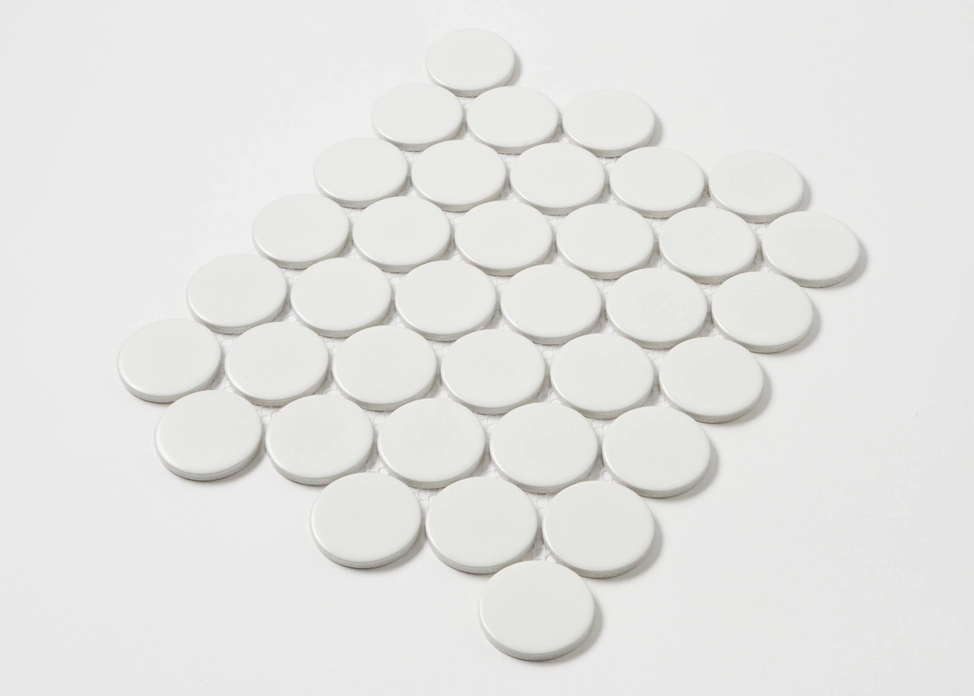 Overhead pack shot of White Matte Porcelain Glazed Penny Round 48mm tiles arranged in a diamond grid pattern showing matte white finish and circular shape.