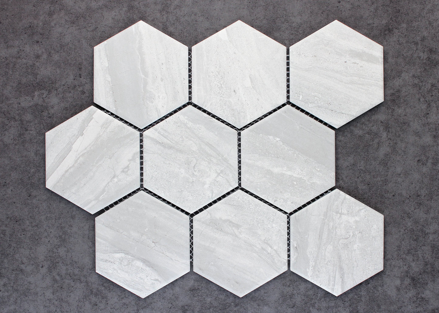 Pack shot of Wooden Grey Matte Porcelain Glazed Hexagon 95x110mm tiles arranged in a seven-piece mesh-backed mosaic sheet, showing soft grey tones and subtle linear stone veining.