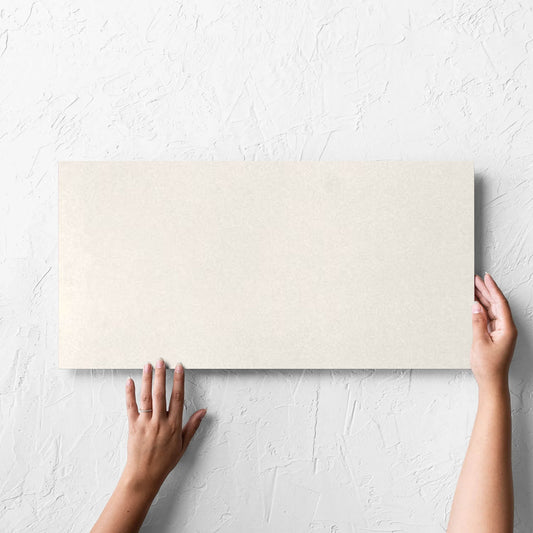 Hand holding a single Yarra Bone Satin 300x600mm tile against a white rendered wall, showing the tile surface