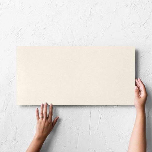 Hand holding a single Yarra Soft Beige Satin 300x600mm tile against a white rendered wall, showing the tile surface