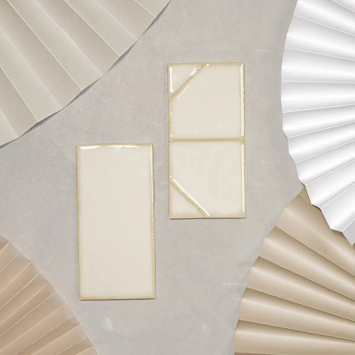 Yoko Daisy Gloss 62.5x125mm ceramic wall tiles in cream white with a shiny glaze finish, displayed alongside pleated paper fan props in neutral tones.