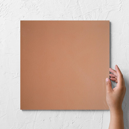 Hand holding a single Yulara Terracotta 300x300mm tile against a white rendered wall, showing the tile surface